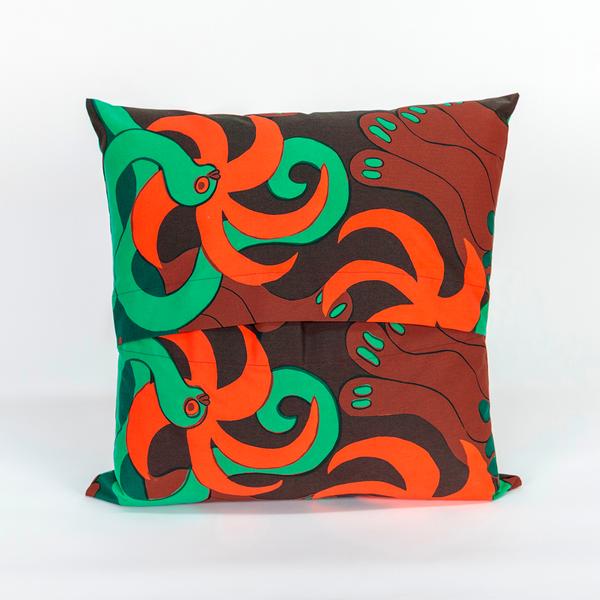 The back of a square pillow made of fabric featuring a repeating textile pattern with stylized green snakes intertwined with abstract brown shapes and bright orange spirals on a dark brown background. The top and bottom panels of fabric overlap in the center to create an opening.