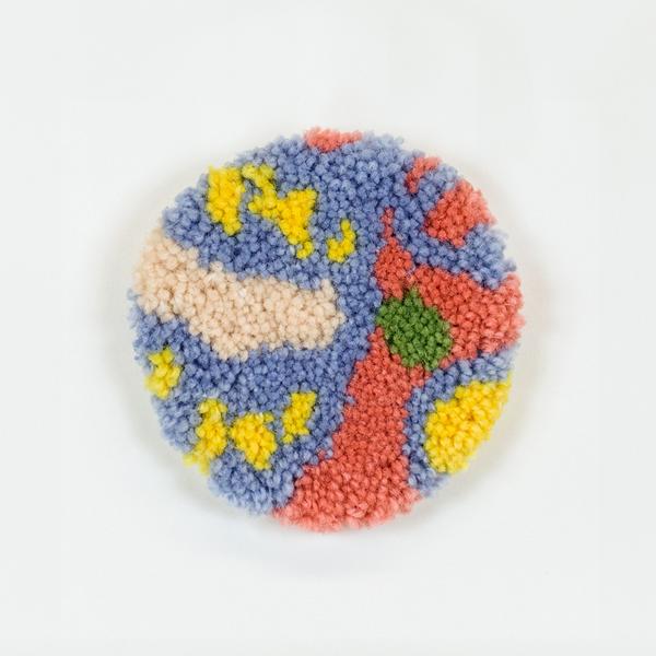 A tufted coaster featuring an abstract design of organic lines and shapes in light blue, pink, yellow, and peach.