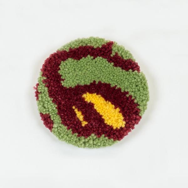 A tufted coaster featuring an abstract design of organic lines and shapes in light green, maroon, and yellow.