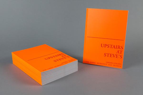A set of bright orange books, some stacked on the left and one on the right standing upright. The lower half of the books read "Upstairs at Steves."