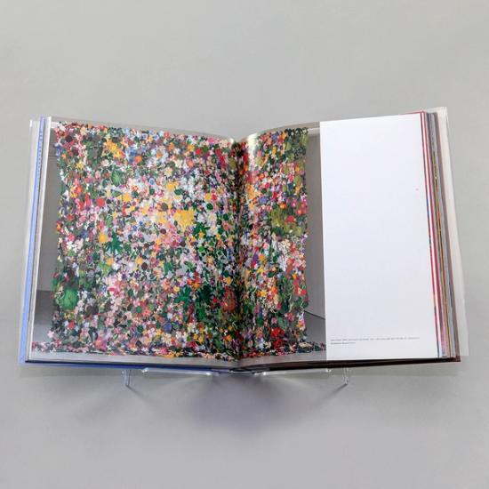 A photo of a book spread with a full-bleed photograph of an artwork by Jim Hodges extending from the left page and over half of the right page. It depicts a sheet-like cascade of tiny colorful flowers and leaves.