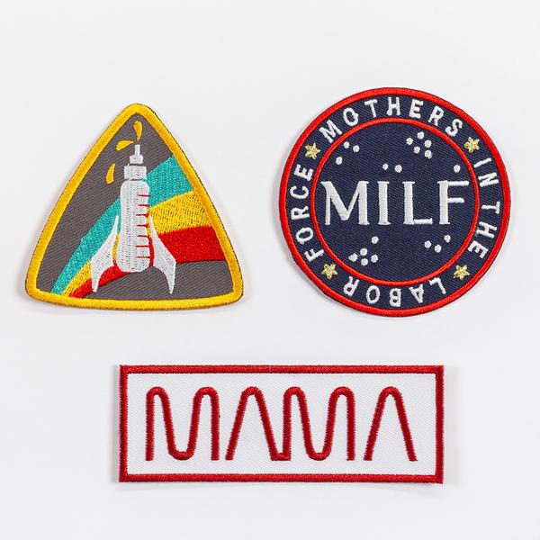 A set of three patches: a triangular patch with rounded corners featuring a baby bottle that looks like a rocket; a circular patch that reads "MILF" and "Mothers in the Labor Force"; and a long rectangular patch that reads "MAMA"