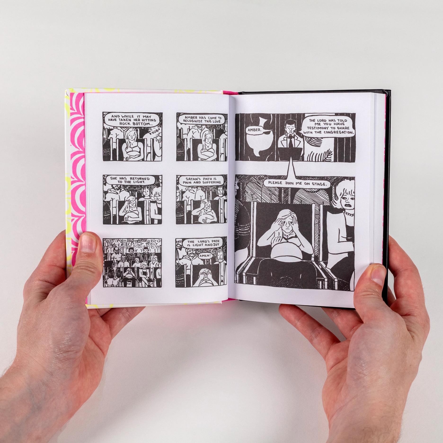 A photograph of two hands holding open a spread from a book. The book features cartoon panels of a character sitting within a church congregation looking embarrassed.