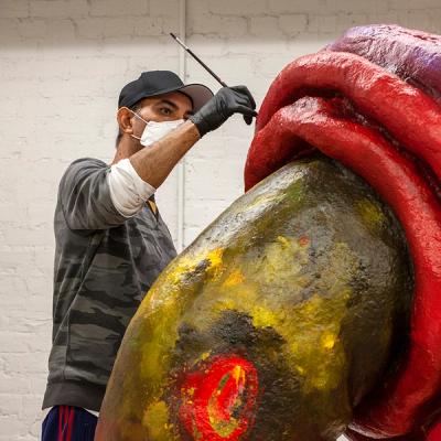 Ahmed Alsoudani painting a sculpture for his exhibition, Bitter Fruit at the Fabric Workshop and Museum. The sculpture is larger than Ahmed and is made up of shades of green, red, and purple
