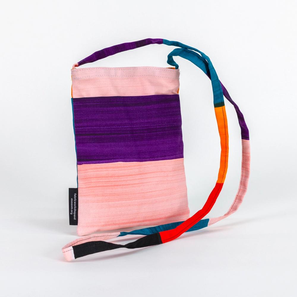 This small, rectangular bag features bold light pink and purple stripes. The thin crossbody length strap has purple, teal, orange, red, black, and light pink bold stripes..