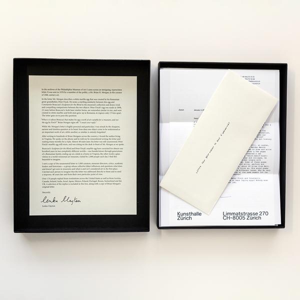 A black box sits open facing up against a white background. Stack of shuffled letters lie within the box's enclosure. On the left is a typed letter signed by the artist, Lenka Clayton. On the right is a stack of papers with an off-white envelope laid overtop. The letter beneath it is marked "Kunsthalle Zurich."