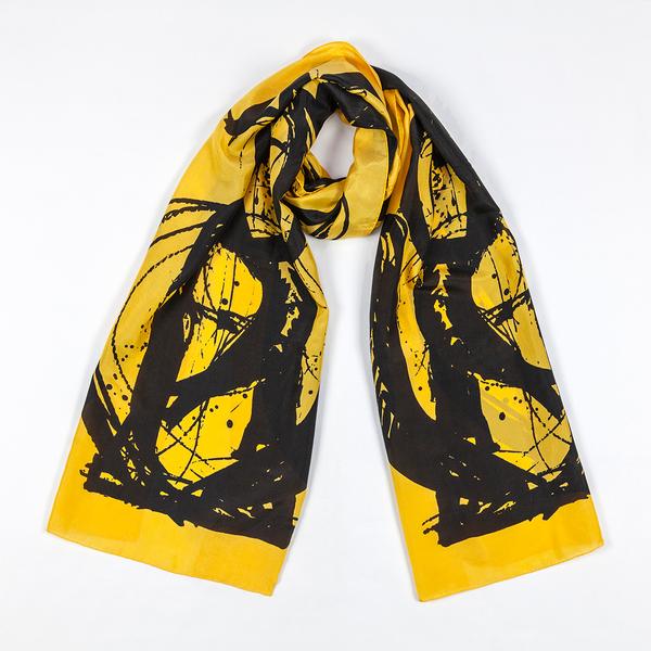 A silk scarf tied in a loose knot and laid against a white ground. This one is bright yellow and features bold, painterly gestures with ink drips and splatters that follow the curving motion of a brush.