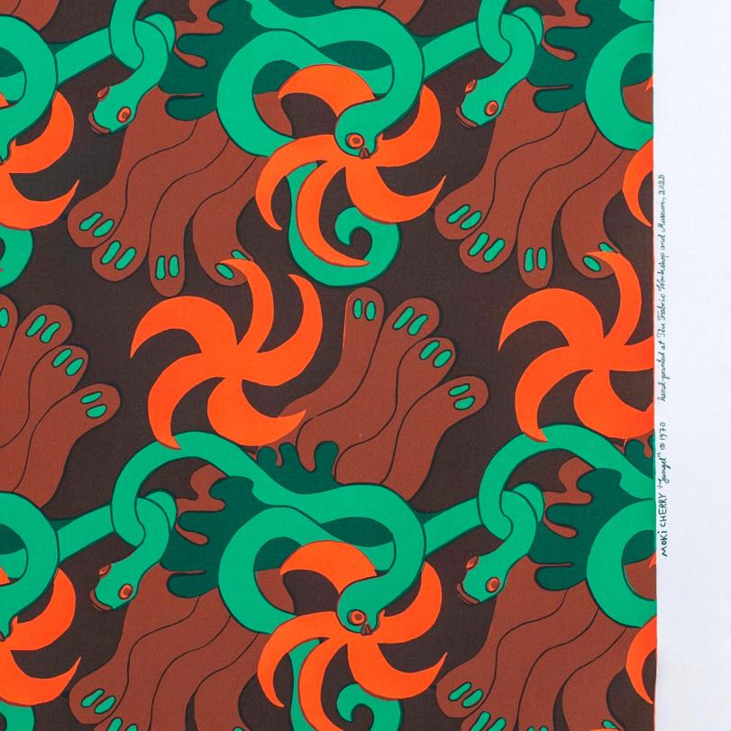 A repeating textile pattern featuring stylized green snakes intertwined with abstract brown shapes and bright orange spirals on a dark brown background printed on white fabric. There is a signature running along the white edge of the fabric.