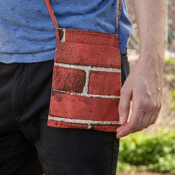 A close up photo of a model's hip wearing a small, rectangular, cross-body bag that features a red brick print.