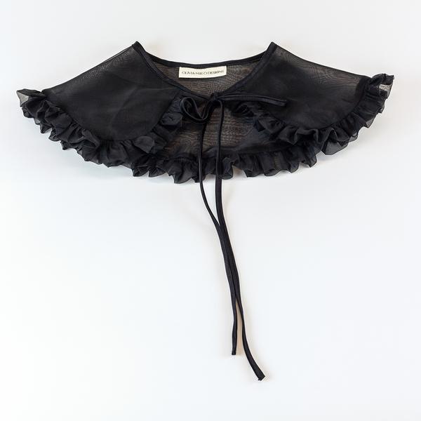 A black silk organza removable collar is lying front facing up, flat against a white background. It is slightly sheer and has a ruffle around the outer edge. The tie is tied in a bow.