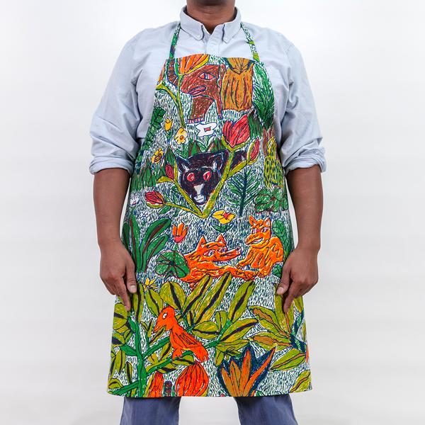 A studio photo of a man wearing a screenprinted apron. The pattern on the apron features a colorful design of hand-drawn leafy foliage, flowers, and wild creatures.