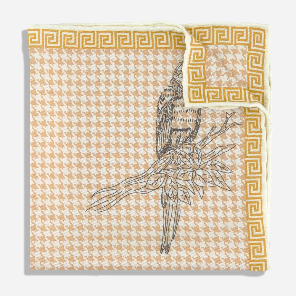 A pocket square with a folded corner. Its gold border resembles a Greek-style spiral frieze. There is a black line illustration of a Kasuku parrot sitting on a leafy branch on a light pink and white houndstooth background.