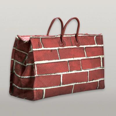 An angled view of a broad handbag featuring a red brick pattern wrapped around all sides. Two sturdy handles form a loop on each side, secured in an ovular pinch over the brick pattern.