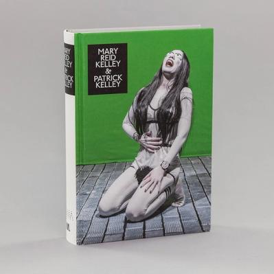 A photo of a book, "Mary Reid Kelley & Patrick Kelley," featuring a kneeling female character who is holding her belly and tilting back in laughter. She has long hair and bug eyes and is rendered in warm grays with black accents. She is posed on gray floorboards against a green background. 