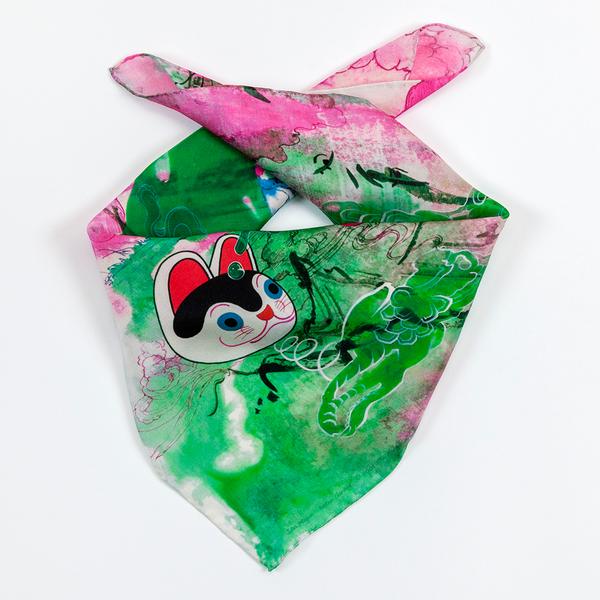 A square scarf folded with its ends crossed, ready to be tied around one's neck. Its image features fluid ink drawings of pink, green, and blue clouds that intersect with drawings of mountains and peonies in an East Asian style. A drawing of a cartoon cat head floats on the center-left.
