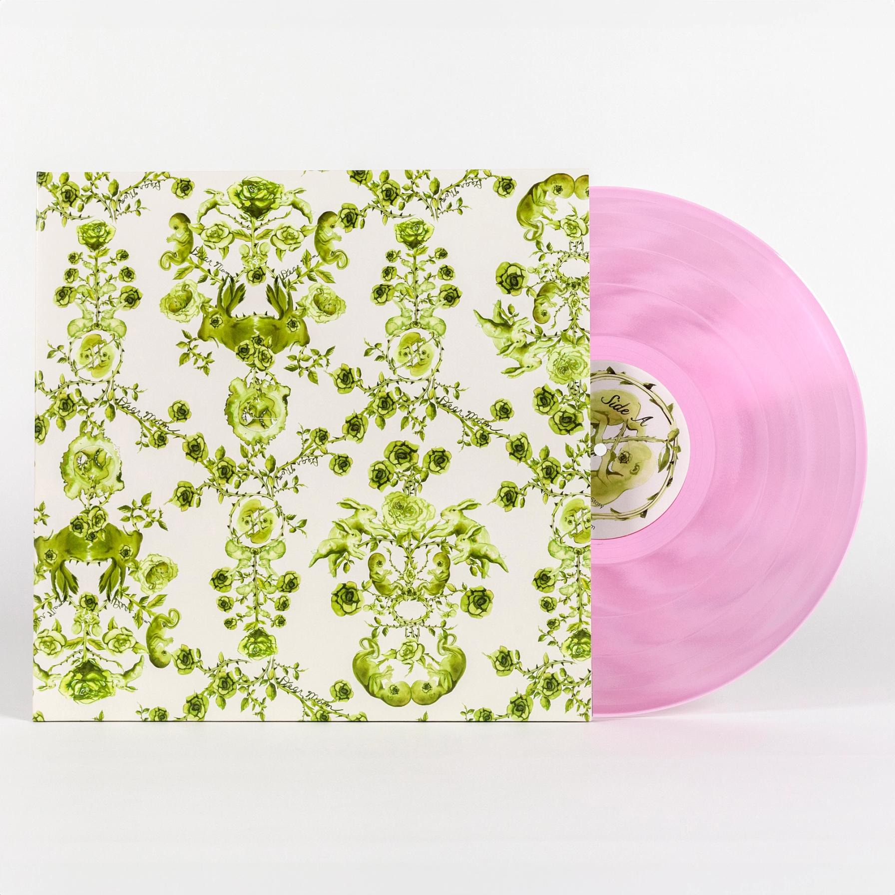 A photo of a vinyl record cover featuring a hand illustrated green toile-like pattern made up mostly of roses but also features twin fetuses and rabbits. This motif is on a solid cream background. Sticking out of the cover is a see-through pink vinyl record that reads "Side A" in the center.