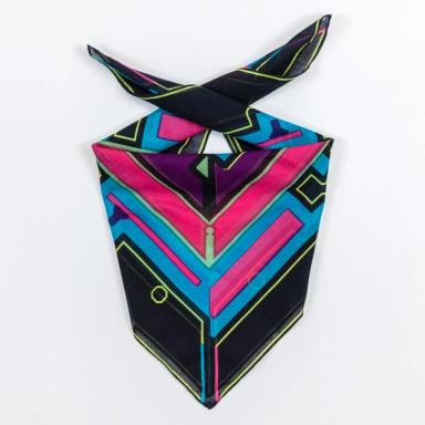 A square scarf folded over with ends ready to be tied around one's neck. This scarf is primarily black, blue, and bright pink, with a purple border around the inner design and neon green accents.