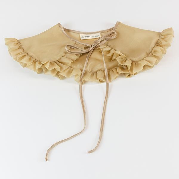 A tan silk organza removable collar is sitting against a white background. The collar has a rounded edge and ruffle going all the way around. The tie is silk and ties in a bow.