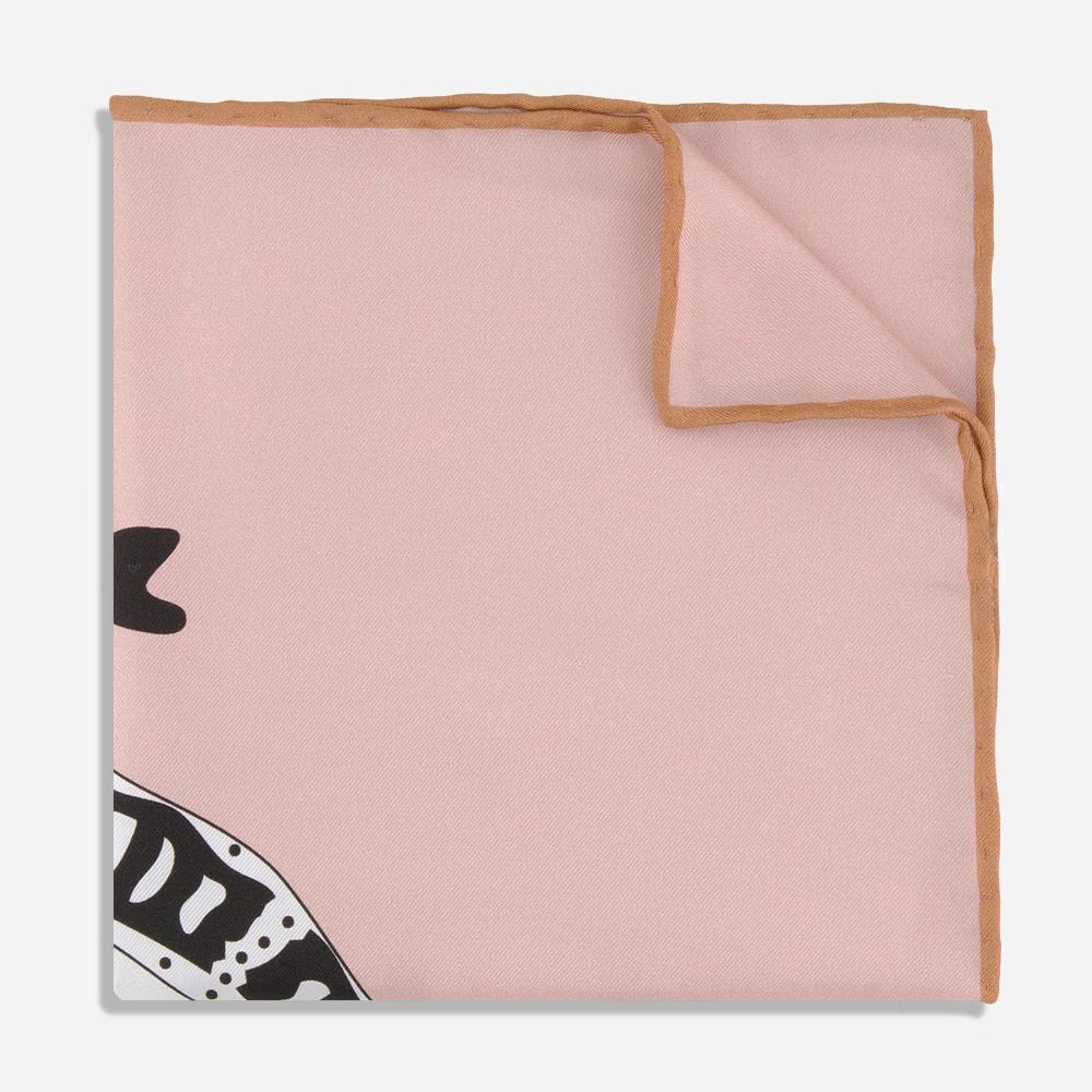 A detail of a folded rose pink silk pocket square with a warm, dark tan bordered seam. There is a glimpse of the printed bold black and white illustration of the Bata bird.