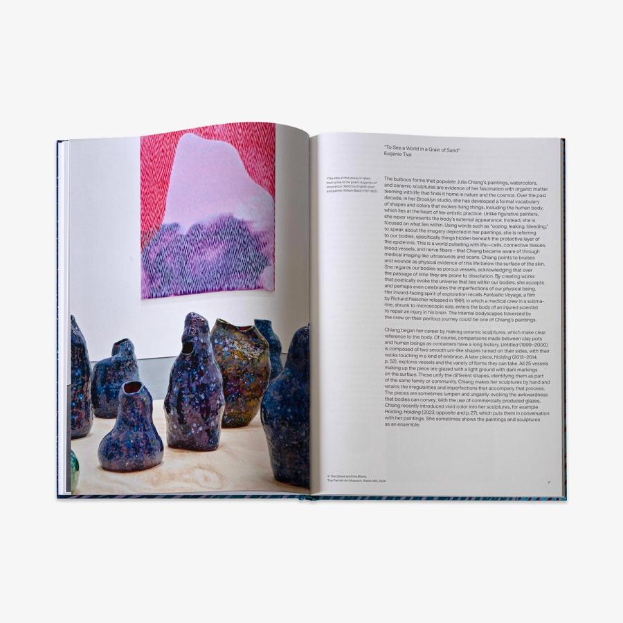 An open book showing a page with a photograph of tall, textured ceramic vessels in mottled colors and a pink-and-purple abstract painting in the background, alongside a page of printed text.