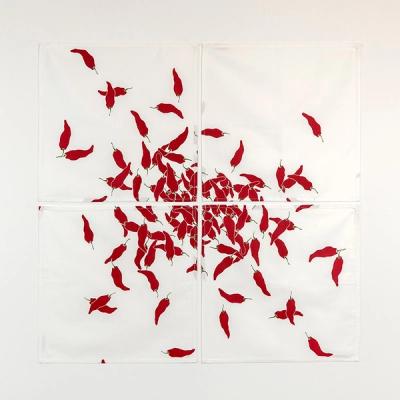 A set of white cotton napkins laid out on a white background. A cascade of overlapping red pepper shapes appear to spill out randomly across the inner corners of four napkins.