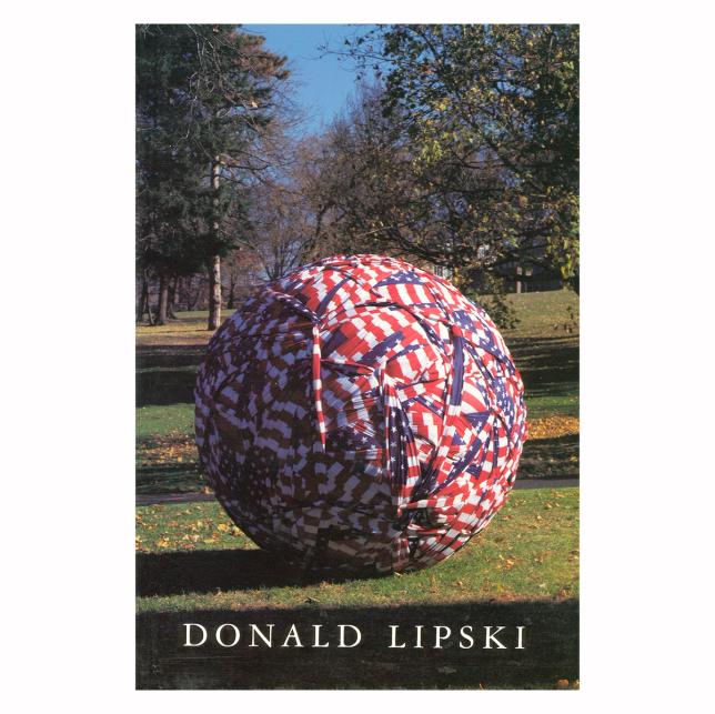 A photo of a book cover by Donald Lipski featuring an 8 foot sized ball wrapped and covered in American flags sitting in a grassy, park-like outdoor environment.