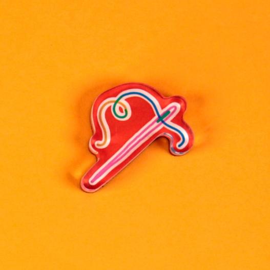 A tool magnet in the form of a red outlined sewing needle and thread is laid out against a bright, warm yellow background. The needle is outlined in pink and the thread wiggles and curls blue, green, and gold.