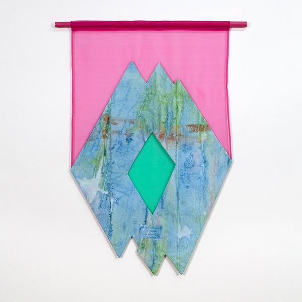 A colorful textile wall hanging with three overlapping diamond-shapes made of fabric that has been dyed in a painterly way in blue, brown and green. Inside there is a sheer green diamond. The overlapping diamonds are framed by a sheer pink fabric background and a pink rod at the top.