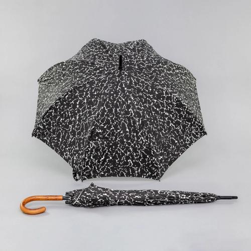 The shell of an umbrella with a black and white speckled pattern faces the viewer. Lying down in front of it is a closed version of the same umbrella that stretches length-wise across the image with its wooden handle curling toward the viewer on the left.