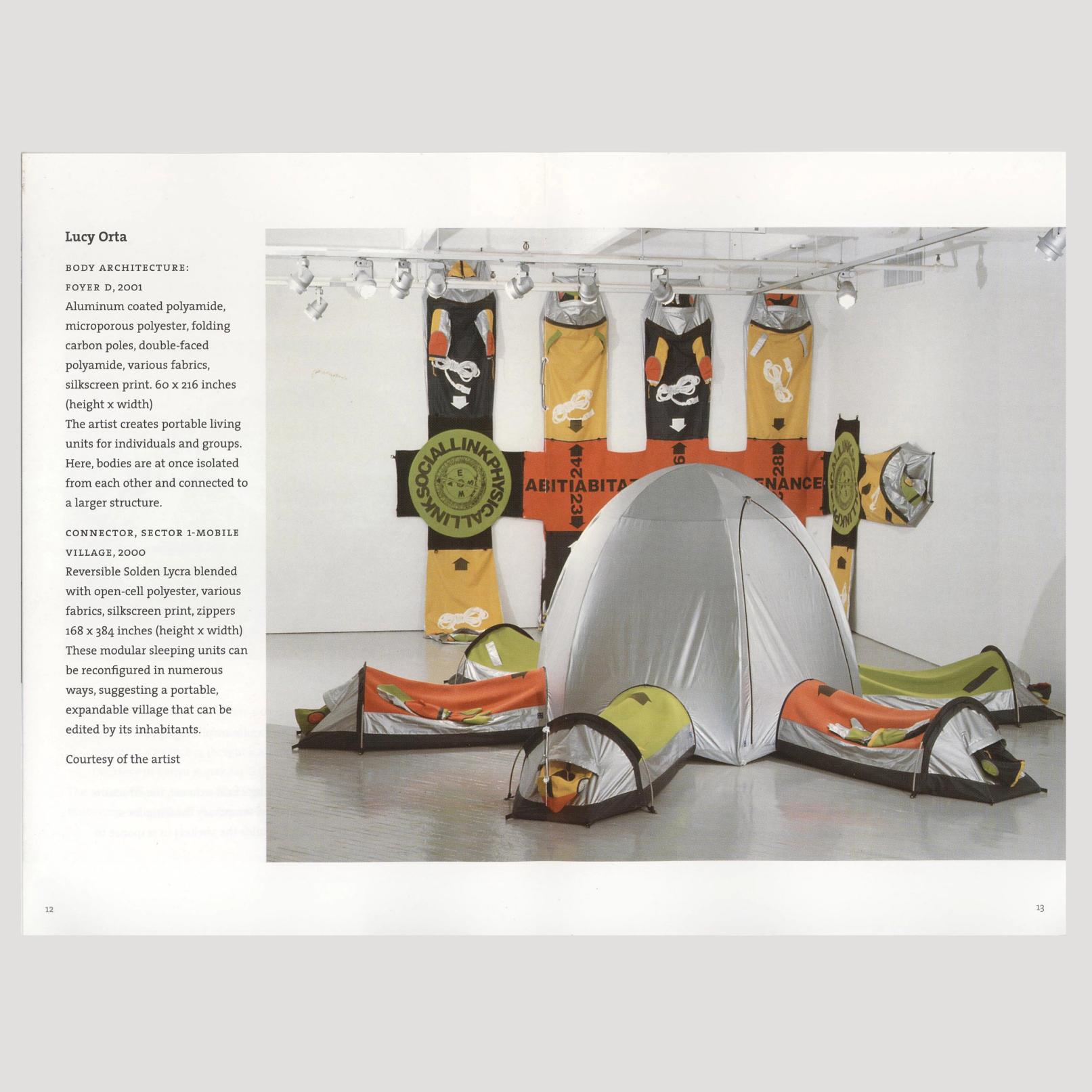 The image is of a book spread with a tall caption on the left and a large image on the right that is positioned over both pages. The image is of a sculpture by Lucy Orta in a gallery. The sculpture is made of fabric and resembles a 7-sided tent. The tent part is tall and silver. Coming out of each side of the tent at the floor are long tubes meant for individual people to lay in. They are silver and have colored tops that alternate between green and orange. Behind the tent hanging on the wall is a large fabric sculpture that spans from the floor to the ceiling in the shape of a 4-pronged picket fence. The caption on the left reads: "Lucy Orta BODY ARCHITECTURE: FOYER D, 2001 Aluminum coated polyamide, microporous polyester, folding carbon poles, double-faced polyamide, various fabrics, silkscreen print. 60 x 216 inches (height x width) The artist creates portable living units for individuals and groups. Here, bodies are at once isolated from each other and connected to a larger structure. CONNECTOR, SECTOR 1-MOBILE VILLAGE, 2000 Reversible Solden Lycra blended with open-cell polyester, various fabrics, silkscreen print, zippers 168 x 384 inches (height x width) These modular sleeping units can be reconfigured in numerous ways, suggesting a portable, expandable village that can be edited by its inhabitants. Courtesy of the artist"