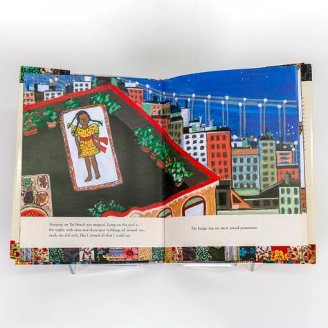 A photograph of an open spread of a picture book by artist Faith Ringgold. The same illustration takes up both pages. The image depicts a girl in a yellow dress sleeping on a rooftop with other tall buildings and the George Washington Bridge in the background against the night sky.