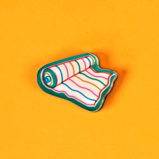 A tool magnet in the form of a green outlined roll of fabric with colorful stripes is laid out against a bright, warm yellow background.