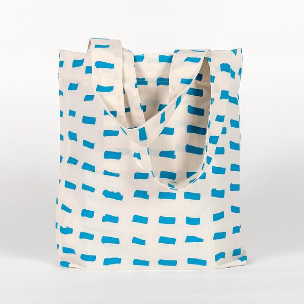 A tall, rectangular tote bag made of white fabric yardage with a printed pattern of short, gestural, brushstroke-like blue dashes.