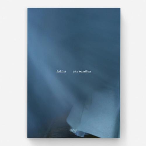 A book cover with varying levels of a smoky blue-gray. The foot of a curtain appears on the lower right. Small text at the center reads "habitus" and "ann hamilton"