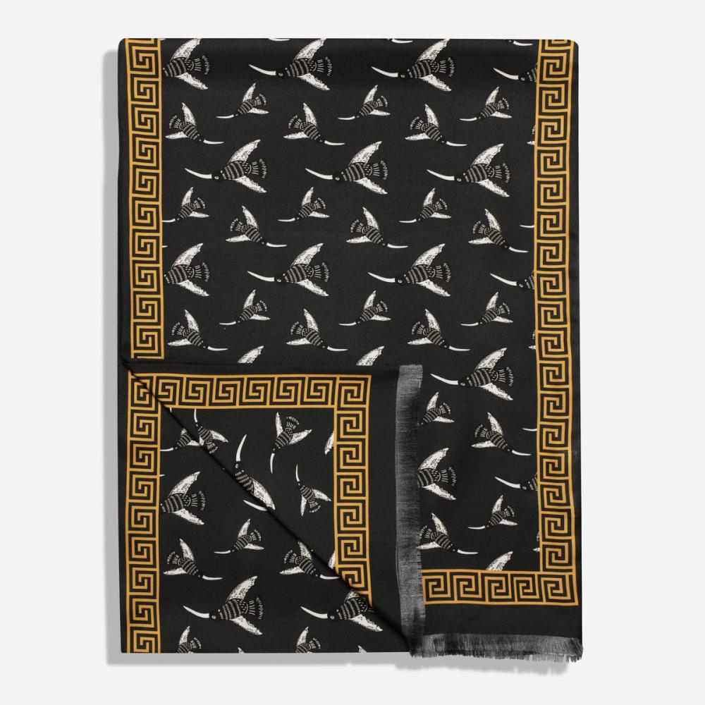 A long scarf folded over in the corner. Its gold border resembles a Greek-style spiral frieze. The interior pattern features illustrated birds with long beaks flying in different directions on a black ground.