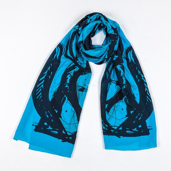 A silk scarf tied in a loose knot and laid against a white ground. This one is light blue and features bold, painterly gestures with ink drips and splatters that follow the curving motion of a brush.