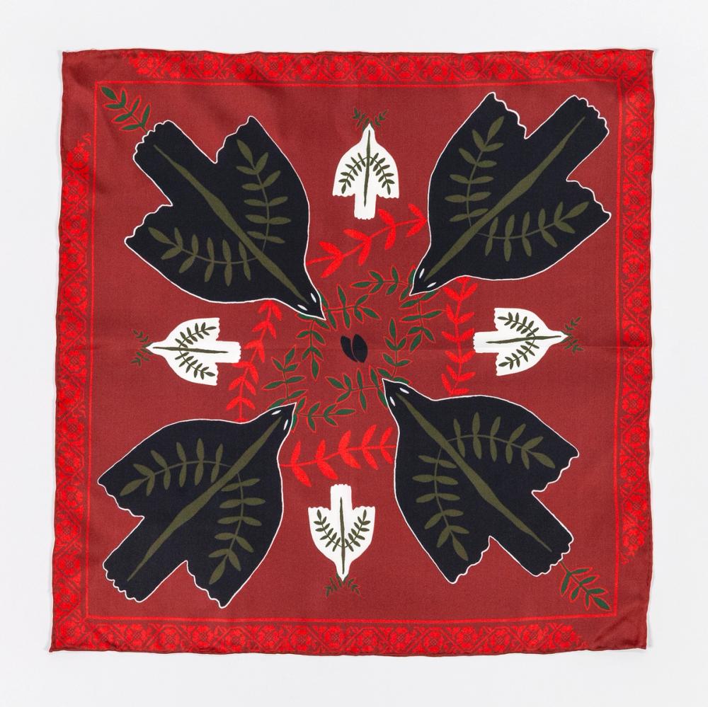 A photograph of a red silk scarf with four black doves in each corner facing the center of the scarf. There are smaller white doves between the black doves facing the edge of the scarf. There is a floral motif as the border of the scarf.