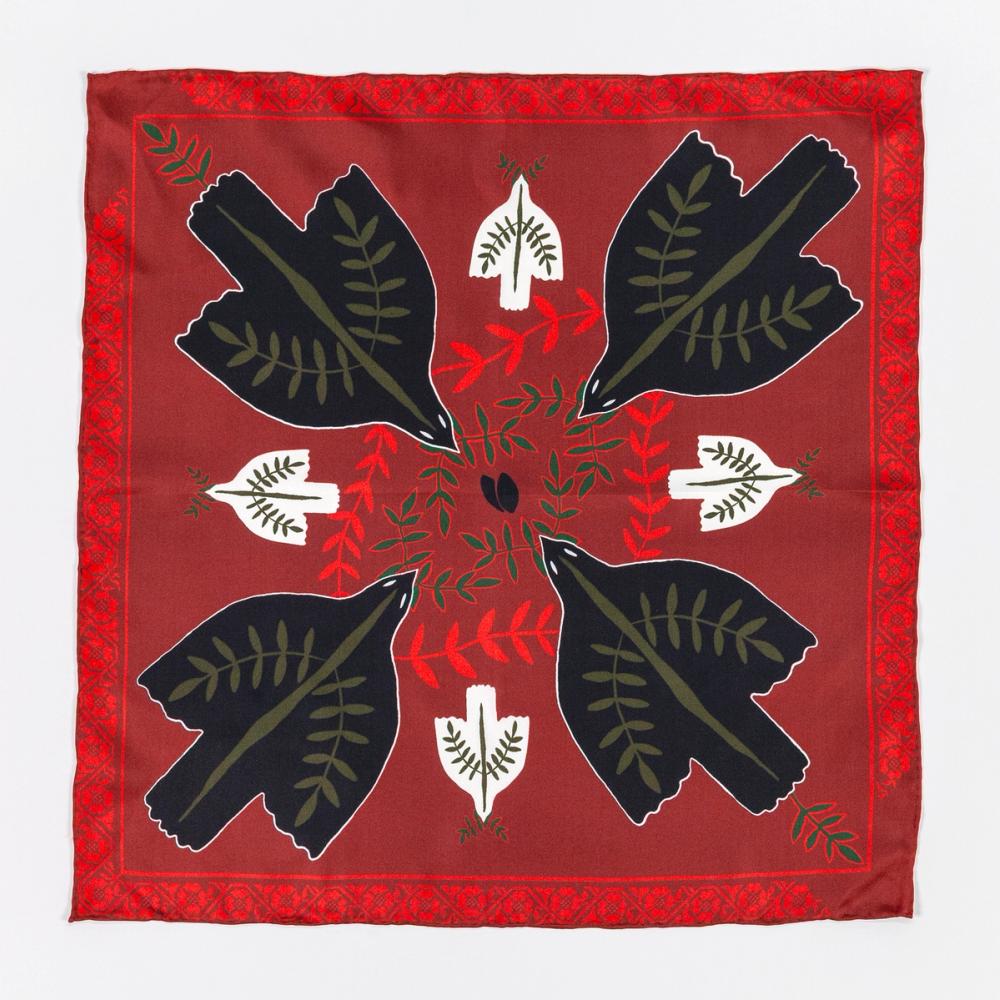 A photograph of a red silk scarf with four black doves in each corner facing the center of the scarf. There are smaller white doves between the black doves facing the edge of the scarf. There is a floral motif as the border of the scarf.