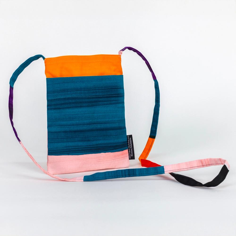 This small, rectangular bag features bold light pink, teal, and orange stripes. The thin crossbody length strap has purple, teal, orange, red, black, and light pink bold stripes..