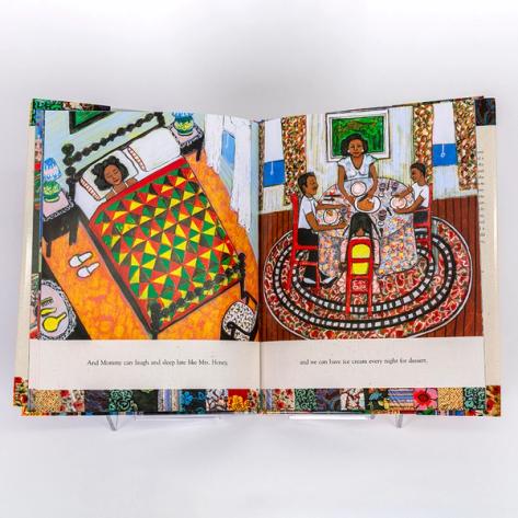 A photograph of an open spread of a picture book by artist Faith Ringgold. On one side there is a colorful illustration of a Black woman is sleeping in bed. On the other side is an illustration of a family of four sitting at a table sharing a meal.