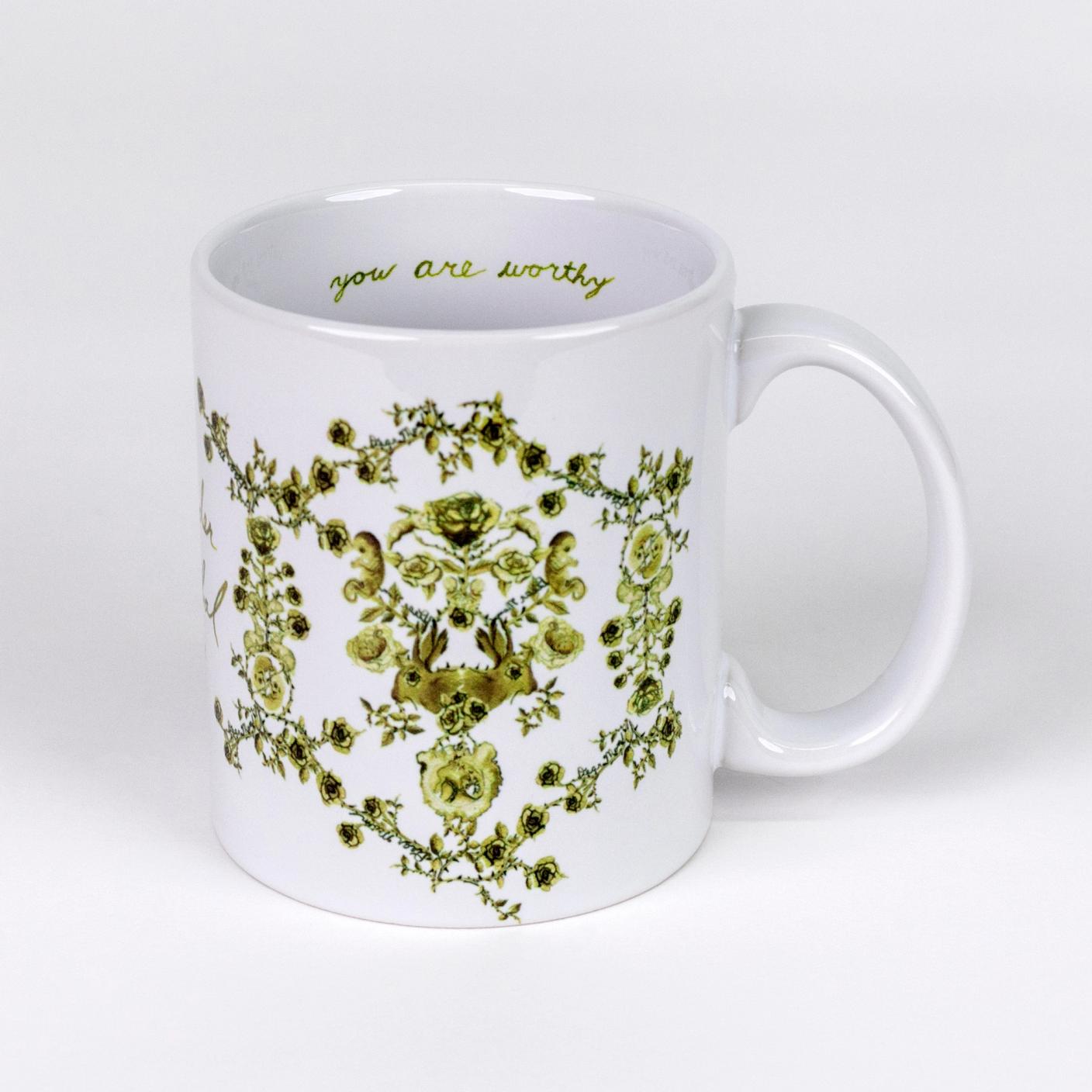 A white ceramic mug featuring a hand illustrated green toile-like pattern made up mostly of roses but also features twin fetuses and rabbits.