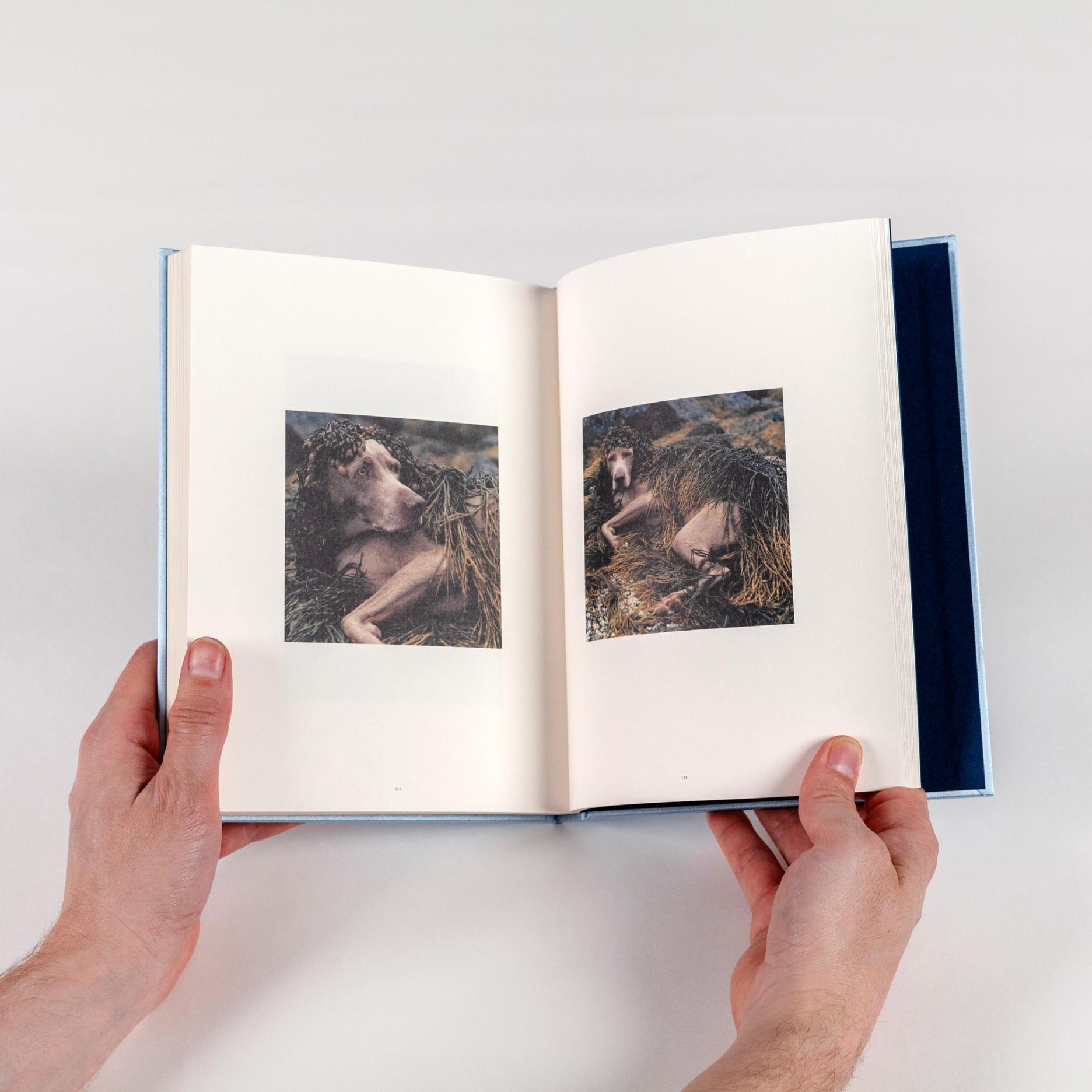 Two hands hold a book open. Two square photographs lie at the center of each page, both featuring a brown down covered in seaweed.