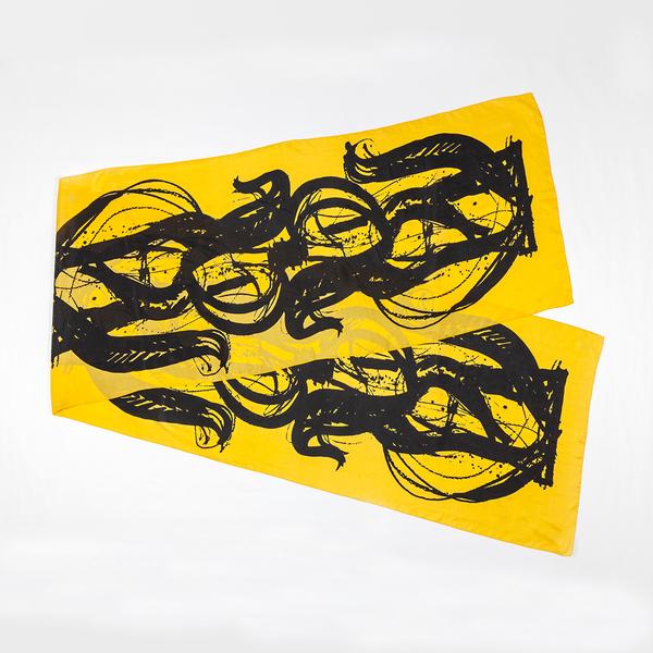 A silk scarf is folded and split diagonally against a white ground. This one is bright yellow and features bold, painterly gestures with ink drips and splatters that follow the curving motion of a brush.