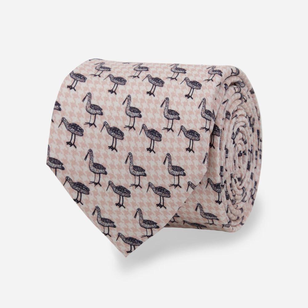 A detail of a rolled up tie with a pattern of black illustrated Bata birds with long beaks in alternating stances on a light pink and white houndstooth background.