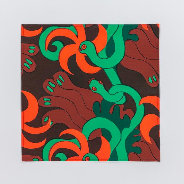 A square napkin made of fabric featuring a repeating textile pattern with stylized green snakes intertwined with abstract brown shapes and bright orange spirals on a dark brown background.