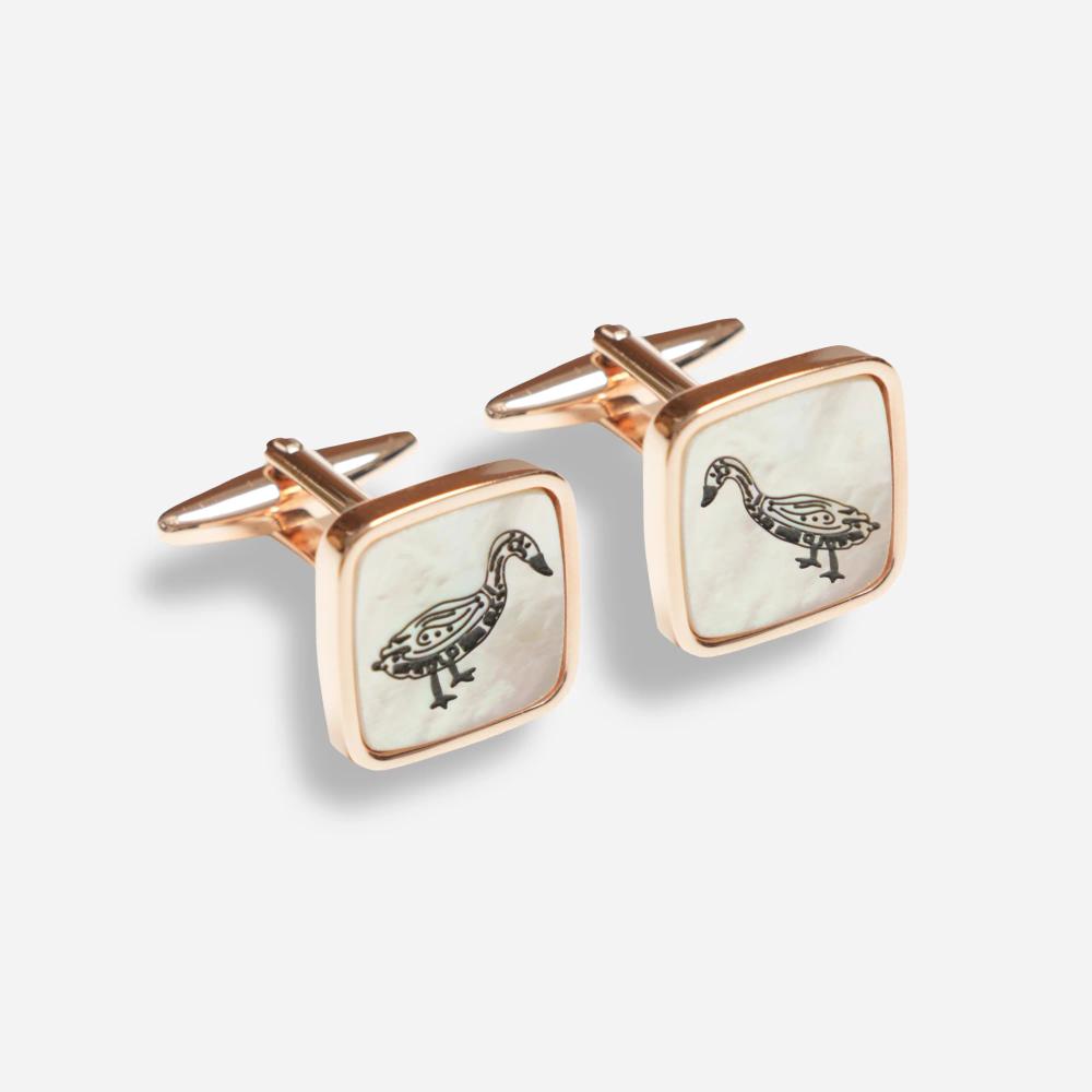 A pair of square white pearlescent cufflinks with a rose gold border and clips. On the pearlescent face is a black line illustration of a Bata bird.