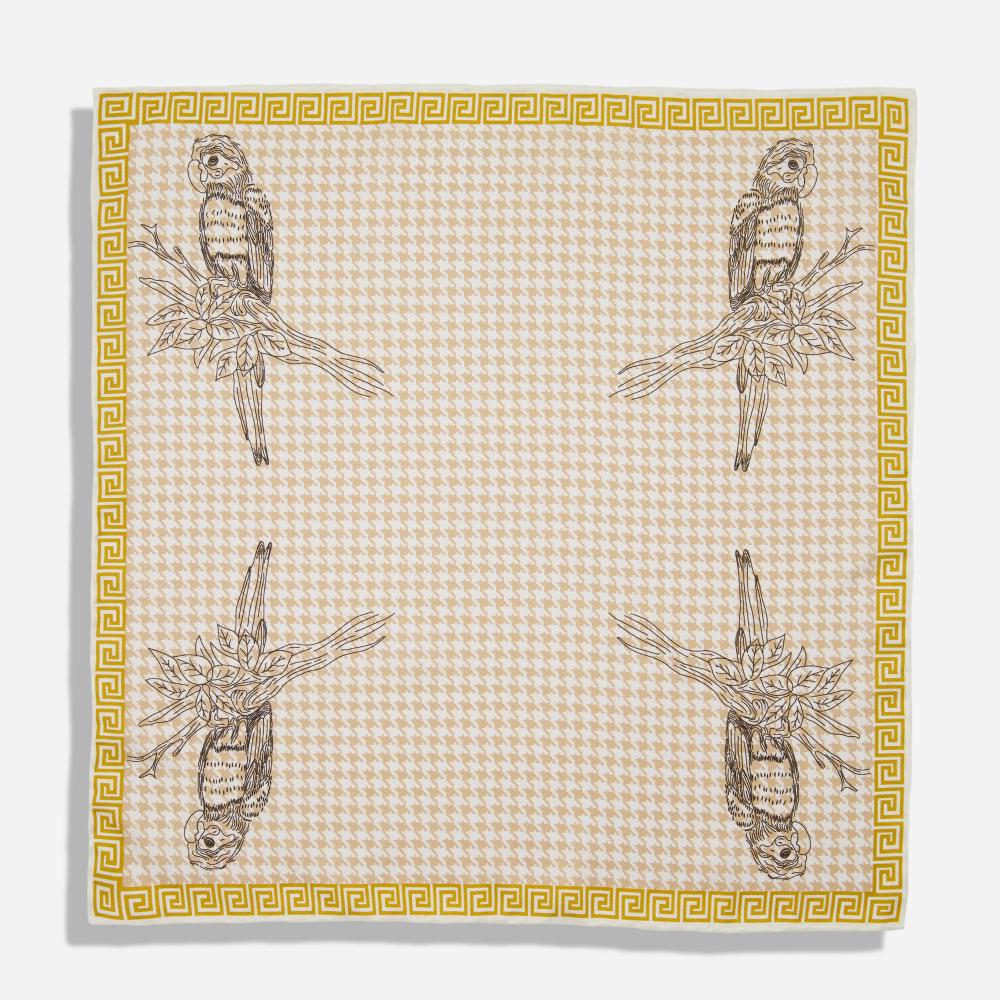 A pocket square with a gold border that resembles a Greek-style spiral frieze. There is are black line illustrations of a Kasuku parrot sitting on a leafy branch in each corner on a light pink and white houndstooth background.