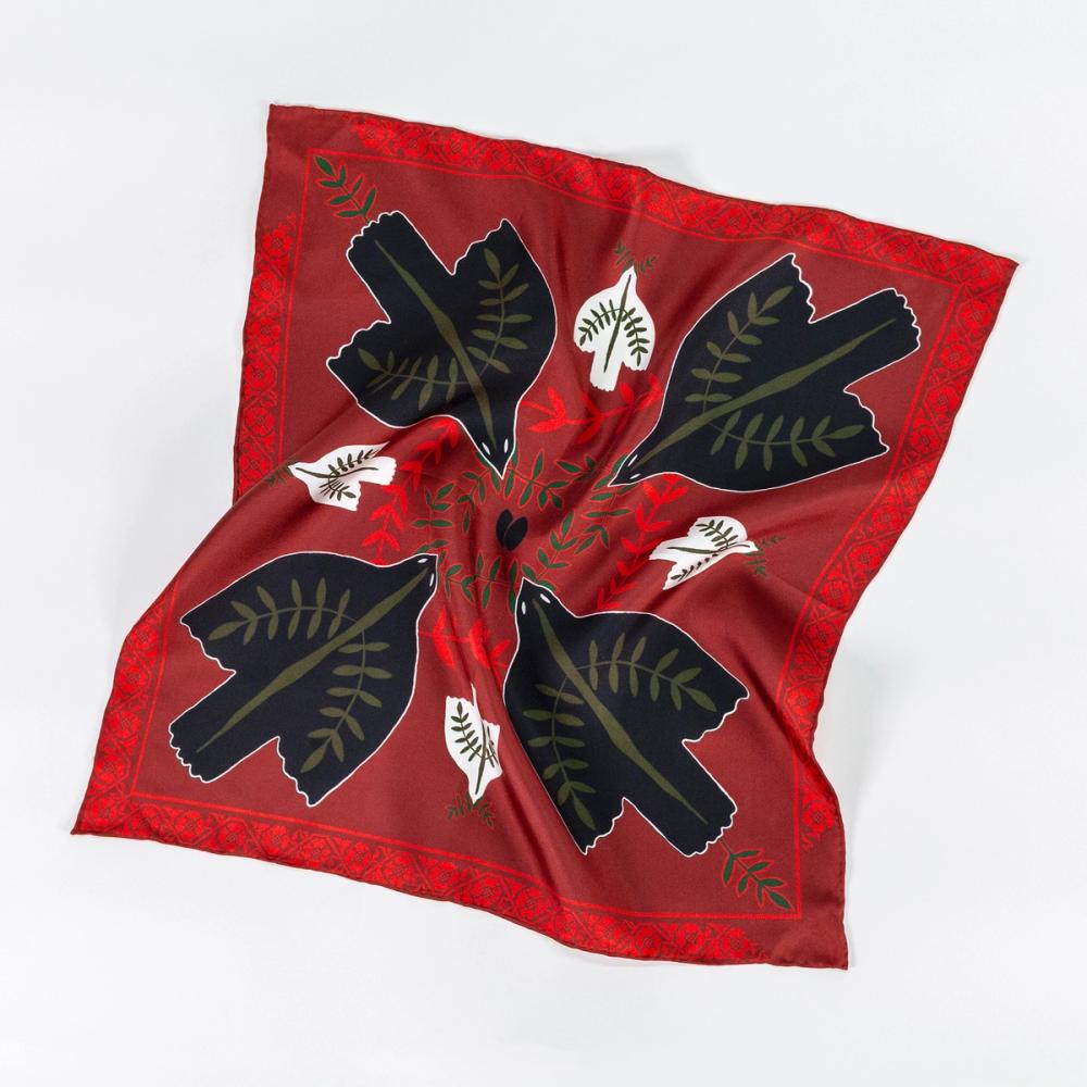 A photograph of a rumpled red silk scarf with four black doves in each corner facing the center of the scarf. There are smaller white doves between the black doves facing the edge of the scarf. There is a floral motif as the border of the scarf.