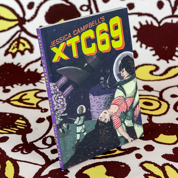 A photograph of a book standing upright against fabric yardage consisting of brown and yellow floral motifs. The book is titled "Jessica Campbell's XTC69" and features a cartoon set in space with an woman astronaut holding a woman in her arms who is wearing a red striped t-shirt rather than a spacesuit.  