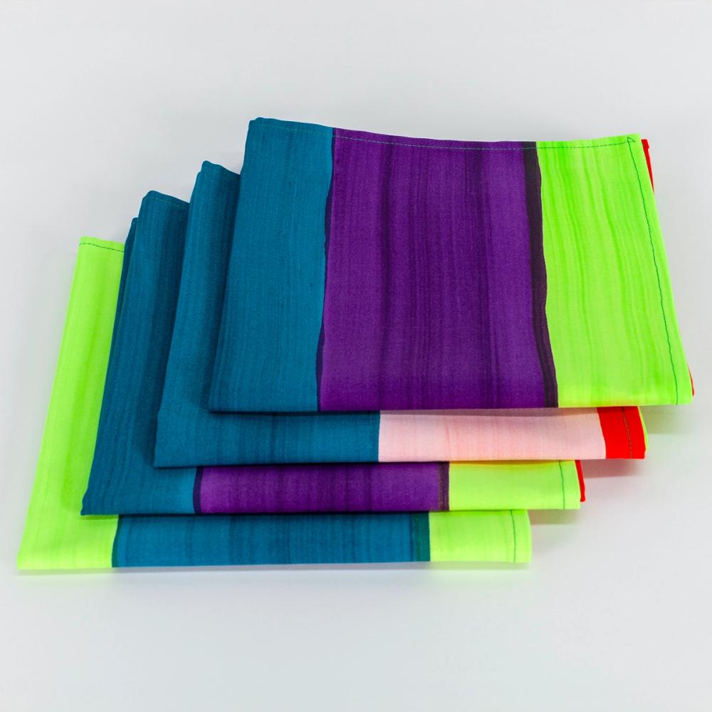 A set of four fabric napkins featuring painted horizontal stripes of alternating light pink, purple, teal, chartreuse, red, and black.  The napkins are folded in squares atop one another.